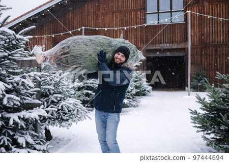 Handsome bearded man holding wrapped Christmas tree on fair. Happy male bring fir tree. Handsome bearded man holding wrapped Christmas tree on fair. Happy male bring fir tree. 97444694