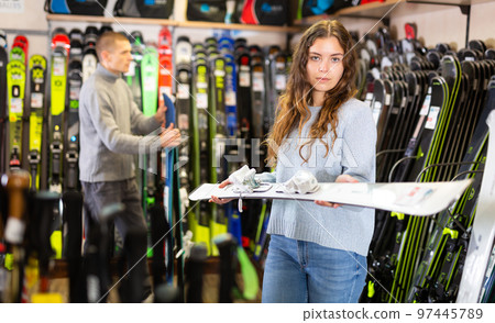 Woman shopper choosing new skis in shop of sports equipment 97445789
