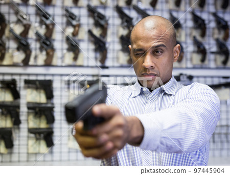 Man takes aim with a pistol in the interior of gun store Man takes aim with a pistol in the interior of gun store 97445904