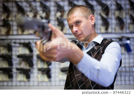 Interested man imitating aiming with pistol in gun shop 97446322