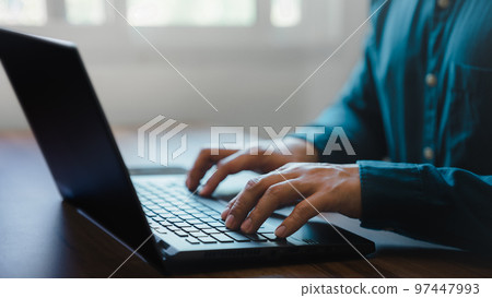 Closeup image of a young man working and typing on laptop computer keyboard on wooden table in cafe. Closeup image of a young man working and typing on laptop computer keyboard on wooden table in cafe. 97447993