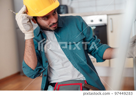 Focused professional worker in uniform is assembling furniture on kitchen. Repair concept 97449283