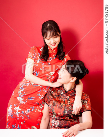Portrait of a smiling daughter and mother in traditional Chinese dress, cuddling against a red background. Portrait of a smiling daughter and mother in traditional Chinese dress, cuddling against a red background. 97451789