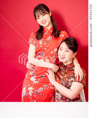 Portrait of a smiling daughter and mother in traditional Chinese dress, cuddling against a red background. Portrait of a smiling daughter and mother in traditional Chinese dress, cuddling against a red background. 97451791