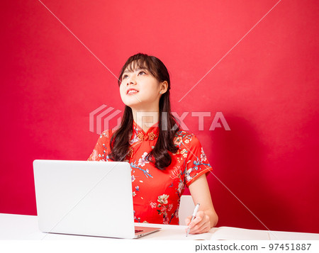 Portrait of young asian woman in traditional cheongsam dress using laptop over red background. 97451887
