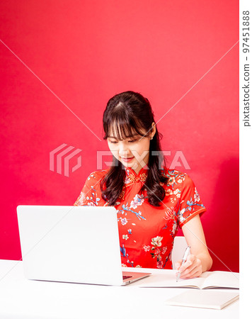 Portrait of young asian woman in traditional cheongsam dress using laptop over red background. 97451888