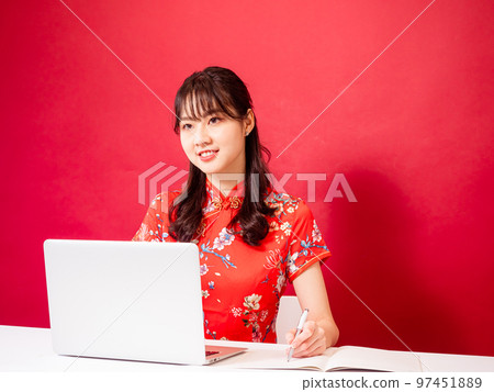 Portrait of young asian woman in traditional cheongsam dress using laptop over red background. Portrait of young asian woman in traditional cheongsam dress using laptop over red background. 97451889
