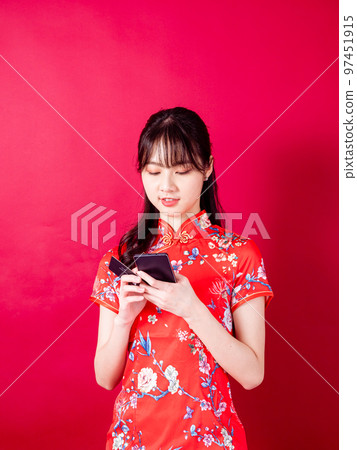 穿著傳統旗袍的年輕亞洲女性在紅色背景上使用智能手機的畫像。 穿著傳統旗袍的年輕亞洲女性在紅色背景上使用智能手機的畫像。 97451915