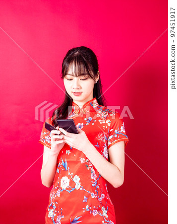 穿著傳統旗袍的年輕亞洲女性在紅色背景上使用智能手機的畫像。 穿著傳統旗袍的年輕亞洲女性在紅色背景上使用智能手機的畫像。 97451917