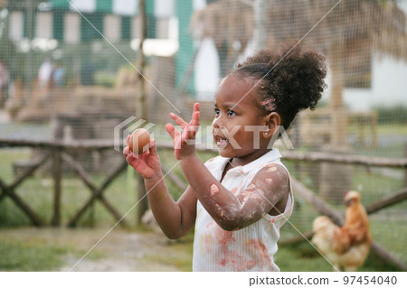 African-American child holding chicken egg with color stain on hand and dress. 97454040