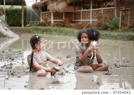 Two happy children child girl catching big frog in the large wet mud puddle on summer day. 97454041