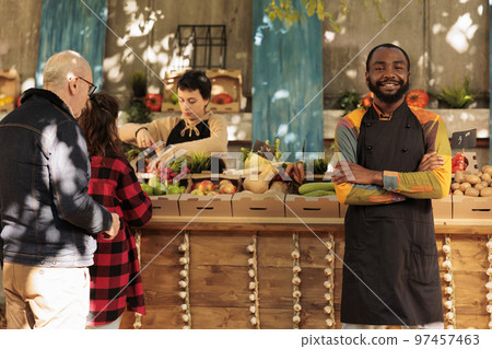 Farmers market vendor standing next to food marketplace stall, selling healthy organic products. Young man with fresh natural fruits and vegetables, seasonal locally grown veggies. 97457463