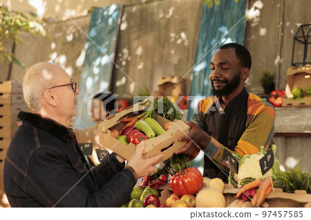 Senior man buying various fresh seasonal fruits and vegetables at farmers market in fall months. Pleasant smiling African American guy small business owner selling his home grown organic produce 97457585