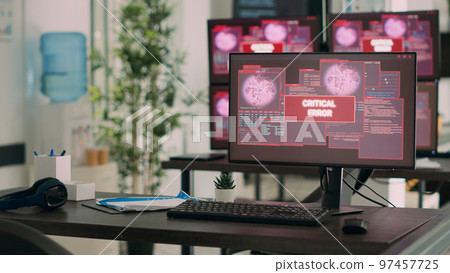 Computers displaying critical error message flashing on screen, dealing with hacking threat and computer malware. Empty desk with multiple monitors showing security breach alert. 97457725