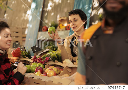 Young female farmer showing various organic fruits to customers at local grocery marketplace. Woman working as vendor holding organic bio homegrown products, fresh seasonal food. Young female farmer showing various organic fruits to customers at local grocery marketplace. Woman working as vendor holding organic bio homegrown products, fresh seasonal food. 97457747