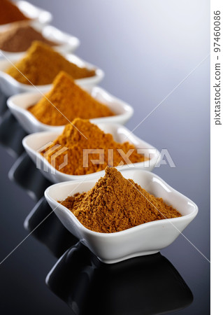 Small white ceramic bowls of Indian spices on black reflective background. Small white ceramic bowls of Indian spices on black reflective background. 97460086