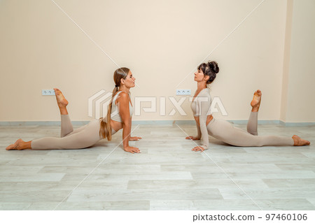 Fitness, pilates stretching exercises, a group of two attractive smiling mature women in beige sports clothes, train in a sports club. Fitness, pilates stretching exercises, a group of two attractive smiling mature women in beige sports clothes, train in a sports club. 97460106