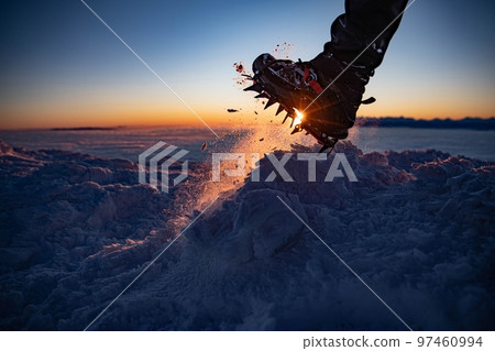 Man in crampon spike boots climbs to the top of a snowy mountain in winter.  97460994