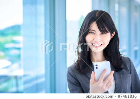 一位穿著西裝的女商人在辦公室走廊裡操作智能手機 一位穿著西裝的女商人在辦公室走廊裡操作智能手機 97461836