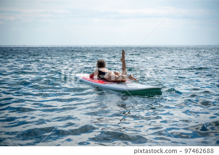 Woman sap sea. Sports girl on a surfboard in the sea on a sunny summer day. In a black bathing suit, he lies on a sap in the sea. Rest on the sea. 97462688