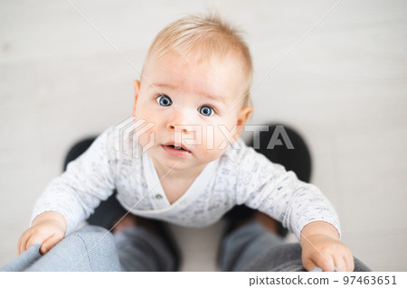 Top down view of cheerful baby boy infant taking first steps holding to father's sweatpants at home. Cute baby boy learning to walk. 97463651