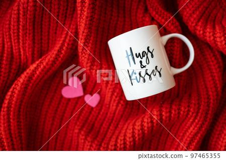 Hugs and kisses inscription on a white cup on a red knitted fabric. Love concept. St. Valentine's Day. 97465355