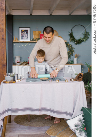 Dad and little son roll out the dough in the kitchen for Christmas ginger cookies or gingerbread house Dad and little son roll out the dough in the kitchen for Christmas ginger cookies or gingerbread house 97467506