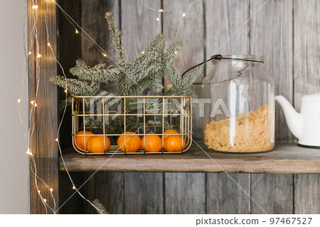 A basket with tangerines and fir branches is on a shelf with kitchen utensils. Christmas home decor 97467527