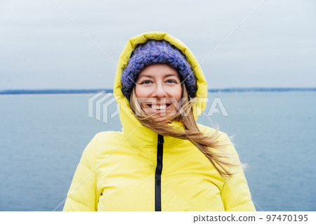 Portrait of happy smiling woman in warm clothes with blown hair enjoying the moment during a walk on the sea coast. Relax and personal fulfillment. Travel in winter. Selective focus. copy space. Portrait of happy smiling woman in warm clothes with blown hair enjoying the moment during a walk on the sea coast. Relax and personal fulfillment. Travel in winter. Selective focus. copy space. 97470195