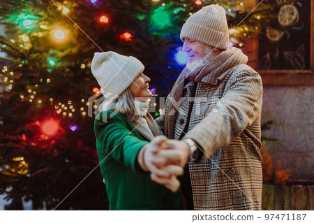 Senior couple having romantic time at outdoor christmas market, dancing near christmas tree. 97471187