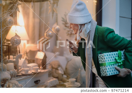 Senior woman looking in window display with Christmas decorations. 97471214