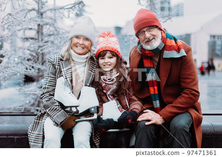 Portrait of seniors and their granddaughter in winter at outdoor ice skating rink. Portrait of seniors and their granddaughter in winter at outdoor ice skating rink. 97471361