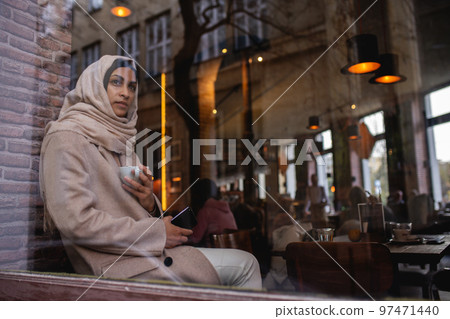 Young muslim woman with smartphone enjoying cup of coffe in cafe. 97471440