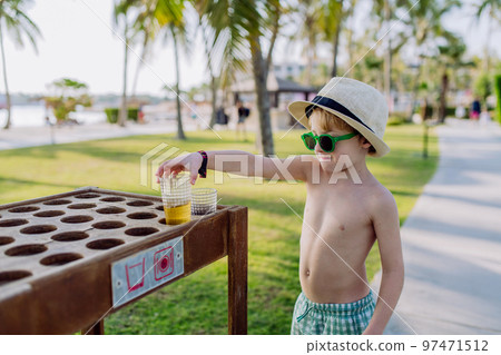 Little boy putting down his drink at storage table on the beach. Little boy putting down his drink at storage table on the beach. 97471512