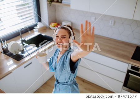 Young woman listening music and enjoying cup of coffee at morning, in her kitchen. Young woman listening music and enjoying cup of coffee at morning, in her kitchen. 97471577