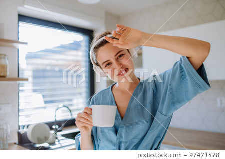 Young woman listening music and enjoying cup of coffee at morning, in her kitchen. 97471578