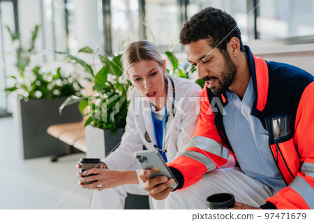 Rescuer having break and talking with doctor colleague, at hospital corridor. 97471679