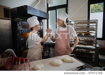 Man with down syndrom helping prepair bread in bakery with his colleague. Concept of integration people with disability into society. Man with down syndrom helping prepair bread in bakery with his colleague. Concept of integration people with disability into society. 97471788