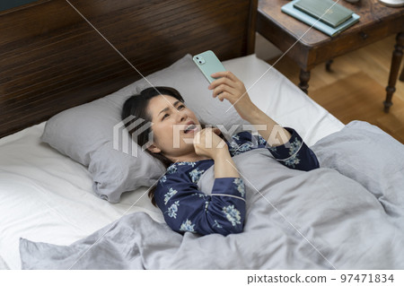 阿拉菲夫女人躺在床上皺著眉頭看著她的智能手機 97471834