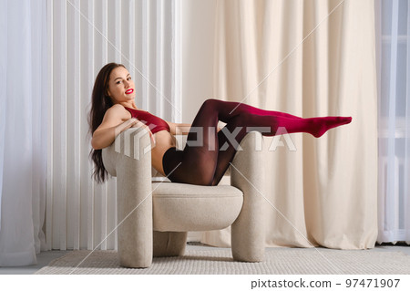 Woman in color gradient opaque pantyhose sitting with her feet on the armrest of the chair 97471907