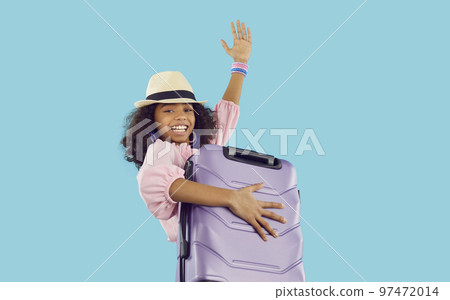 Cheerful funny african american preteen girl holding heavy suitcase and waving her hand. 97472014