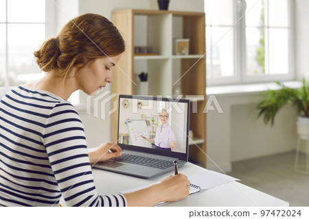 Young woman taking notes during webinar or online class with remote English teacher 97472024