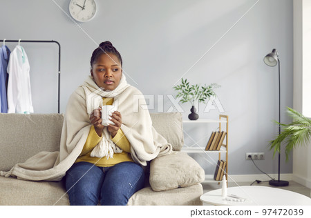 Sick young african-american woman feels unwell and drinks hot drink. 97472039