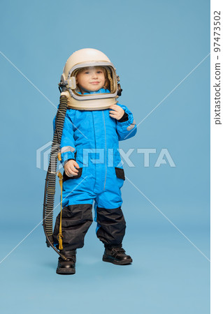 Portrait of little boy, child posing in astronaut costume over blue studio background. Space researcher 97473502