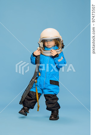 Portrait of little boy, child posing in astronaut costume over blue studio background. Fantastic game. Concept of childhood, emotions 97473507