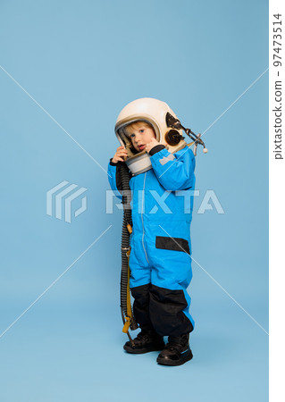 Portrait of little boy, child posing in astronaut costume over blue studio background. Spaceman. Concept of childhood, emotions Portrait of little boy, child posing in astronaut costume over blue studio background. Spaceman. Concept of childhood, emotions 97473514