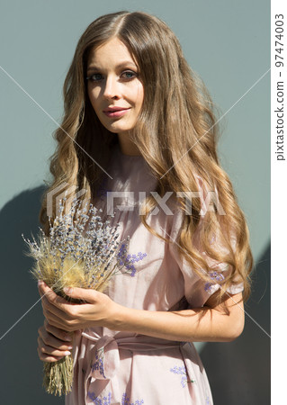 Portrait of a beautiful girl with flowing curly hair, smiling, looking at the camera on the street. Walking around the city, with a bouquet of lavender in your hands. High quality photo Portrait of a beautiful girl with flowing curly hair, smiling, looking at the camera on the street. Walking around the city, with a bouquet of lavender in your hands. High quality photo 97474003