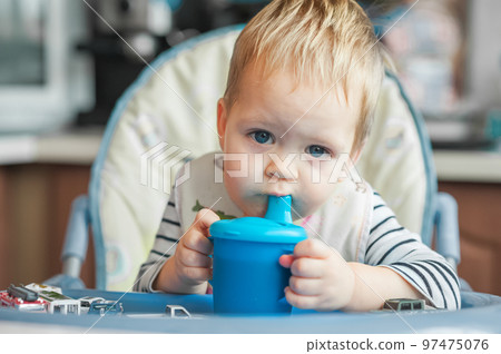 Toddler boy drinks from cup in high chair. Toddler boy drinks from cup in high chair. 97475076