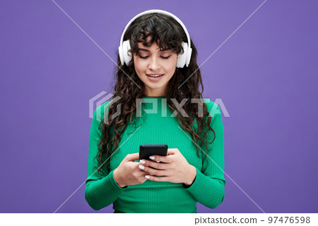 Pretty girl with dark long wavy hair scrolling through playlist in mobile phone 97476598
