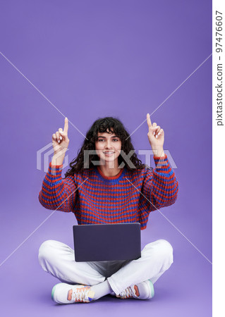Happy young brunette woman with laptop pointing upwards 97476607